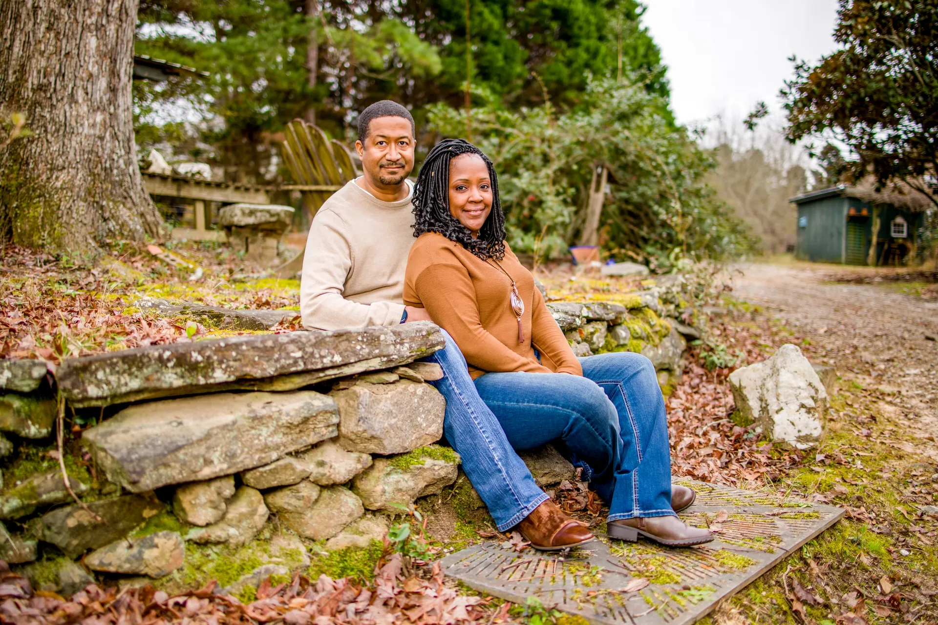 A couple seated close on a low stone wall along a leafy park path in autumn.