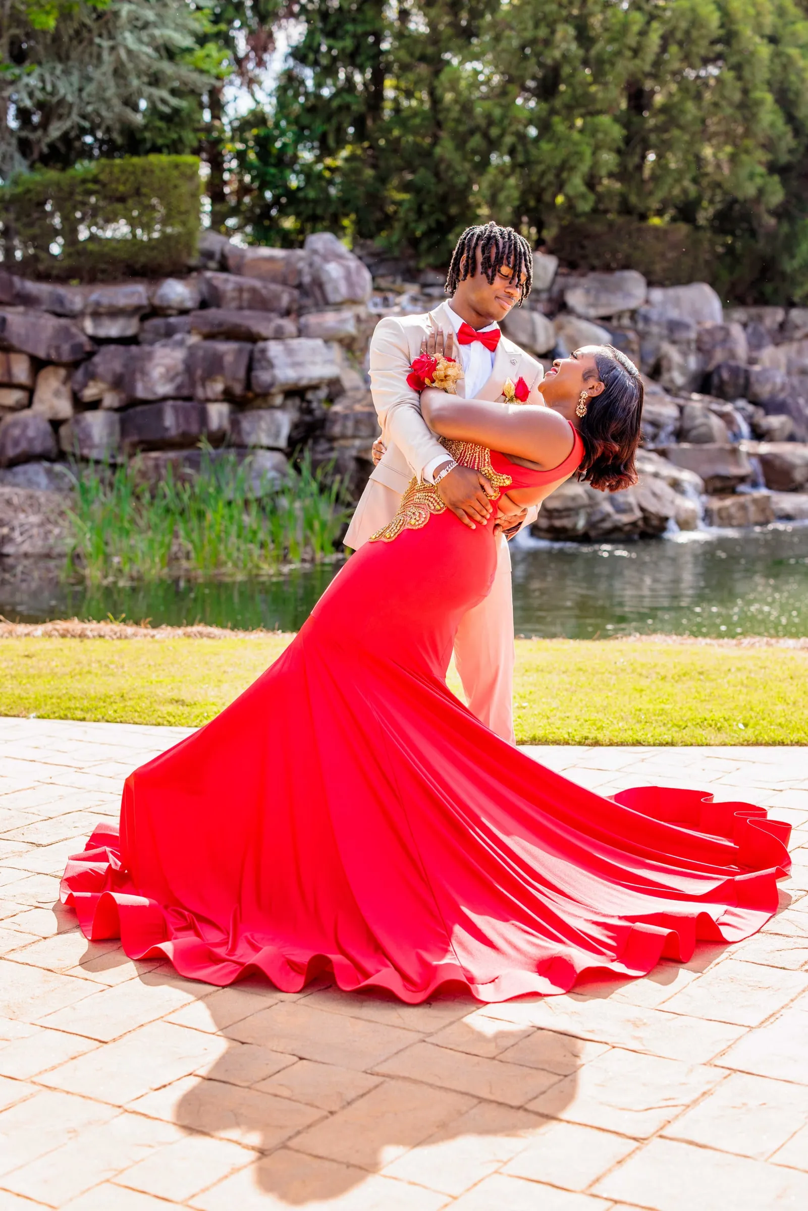 A prom couple dipped mid-pose, her red gown fanning out beside a rock garden pond.