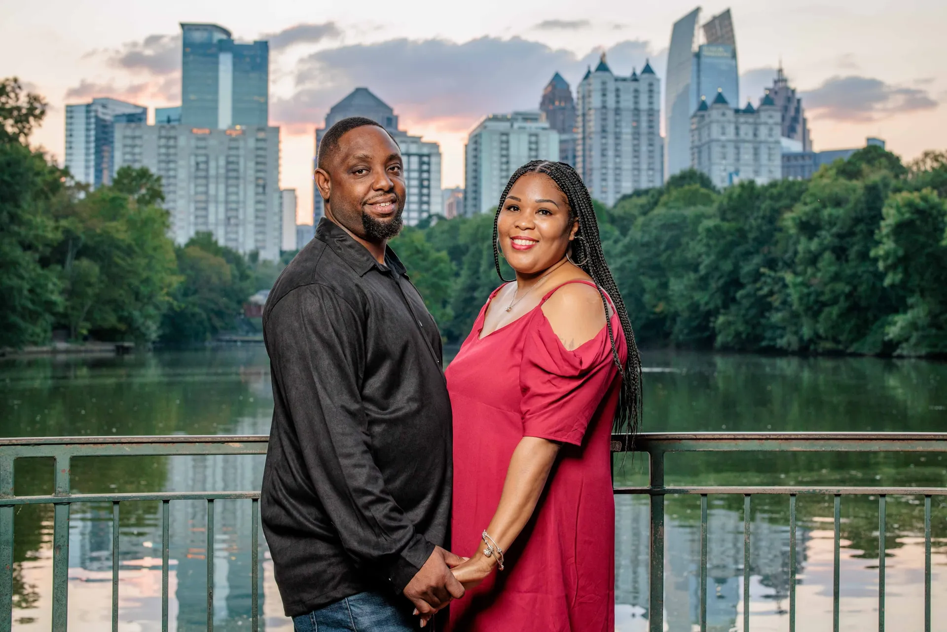 A couple holding hands at the Piedmont Park lake, the Midtown Atlanta skyline glowing behind them.