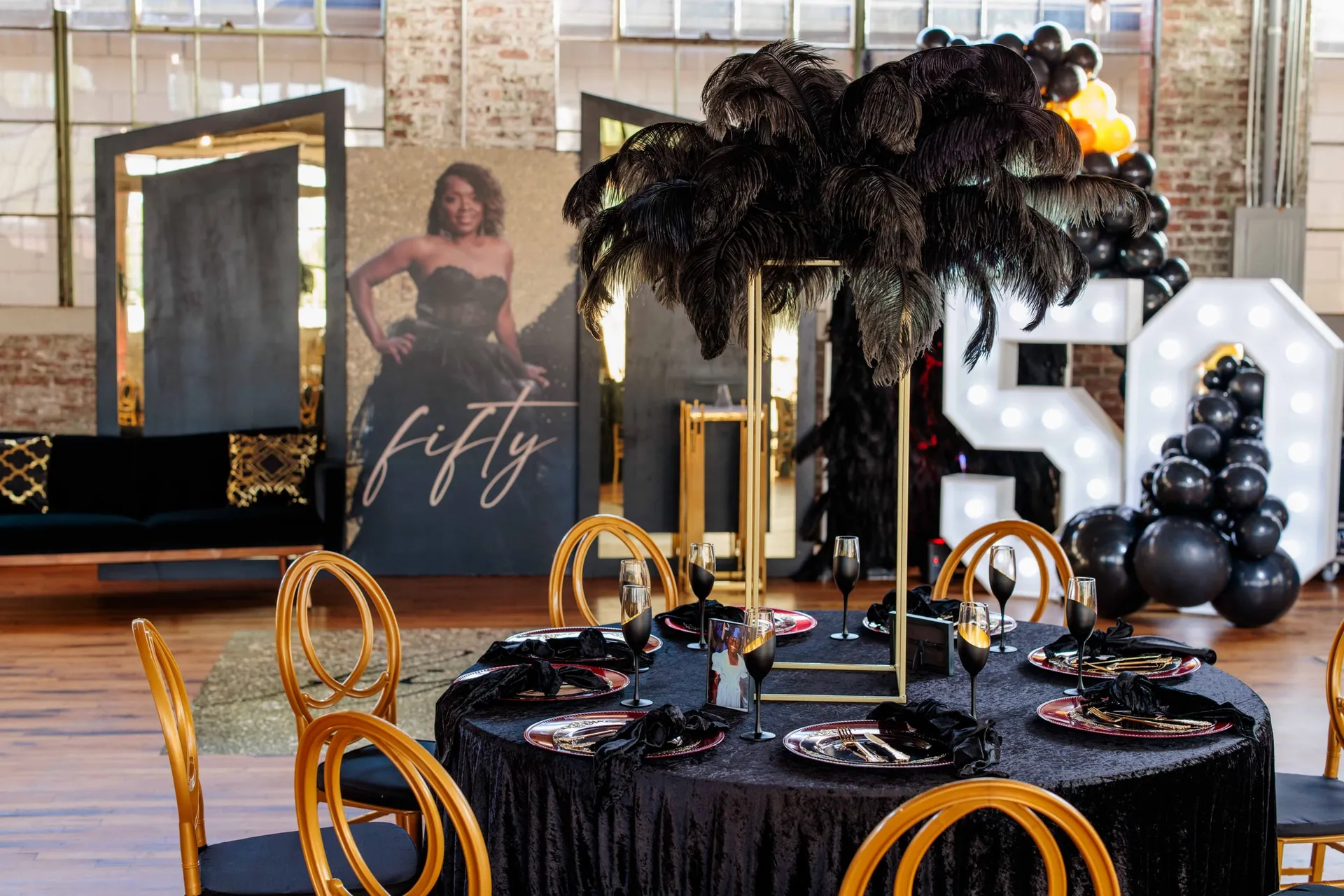 A black and gold table with a feather centerpiece before a lit 50 and a portrait.