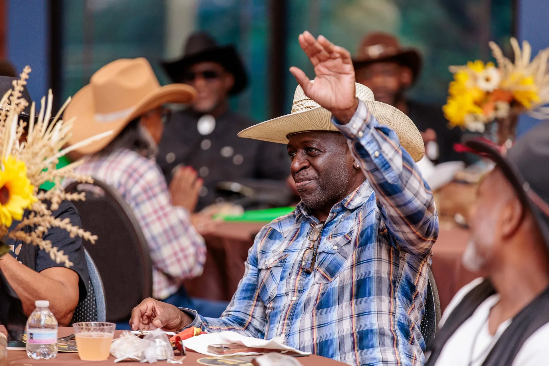 A guest in a cowboy hat and plaid shirt waving from his western party table.