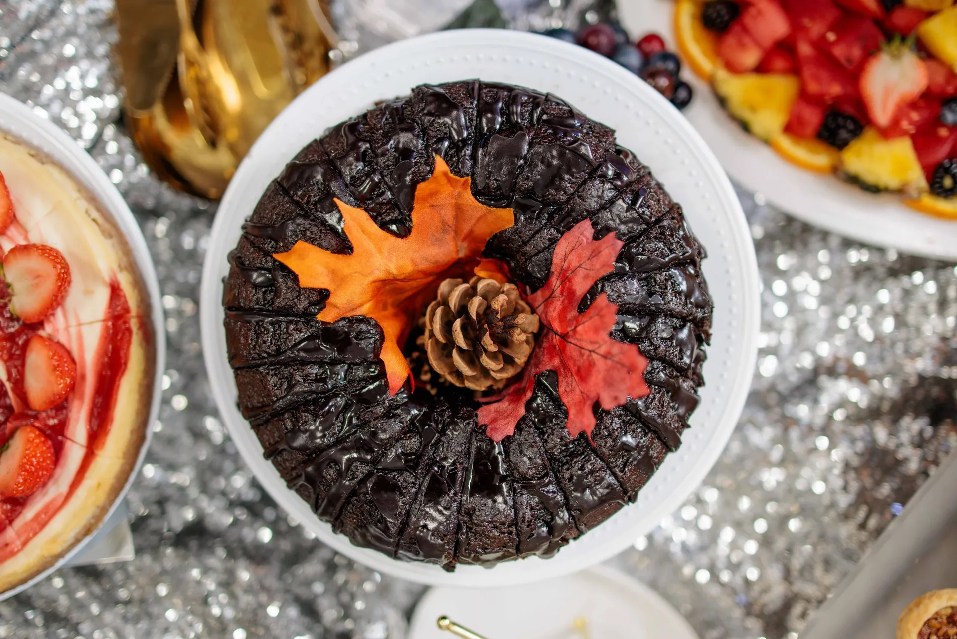 A chocolate cake dressed with an autumn leaf and pine cone on a sequinned dessert table.