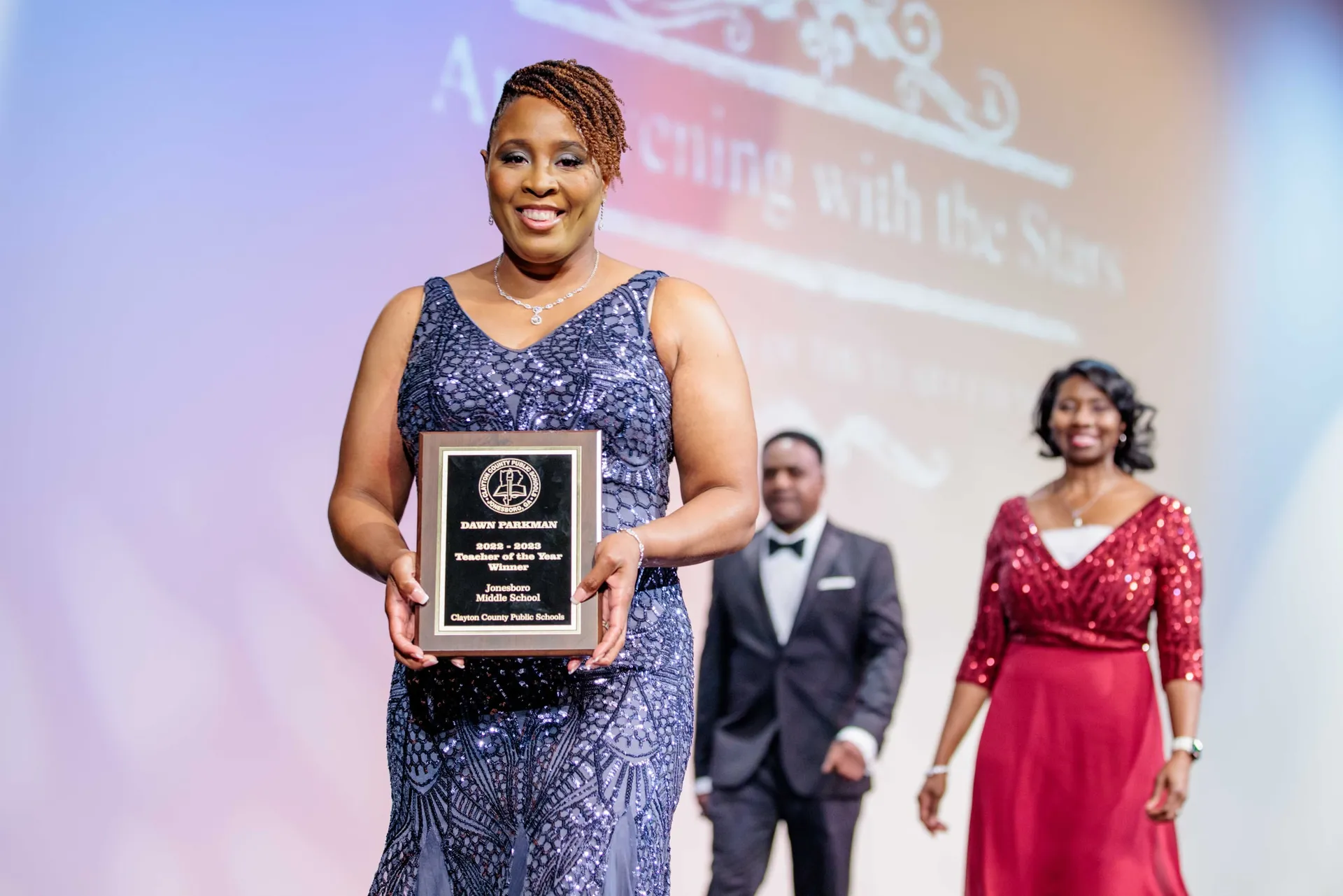 A Teacher of the Year winner holding her plaque on stage at an awards evening.