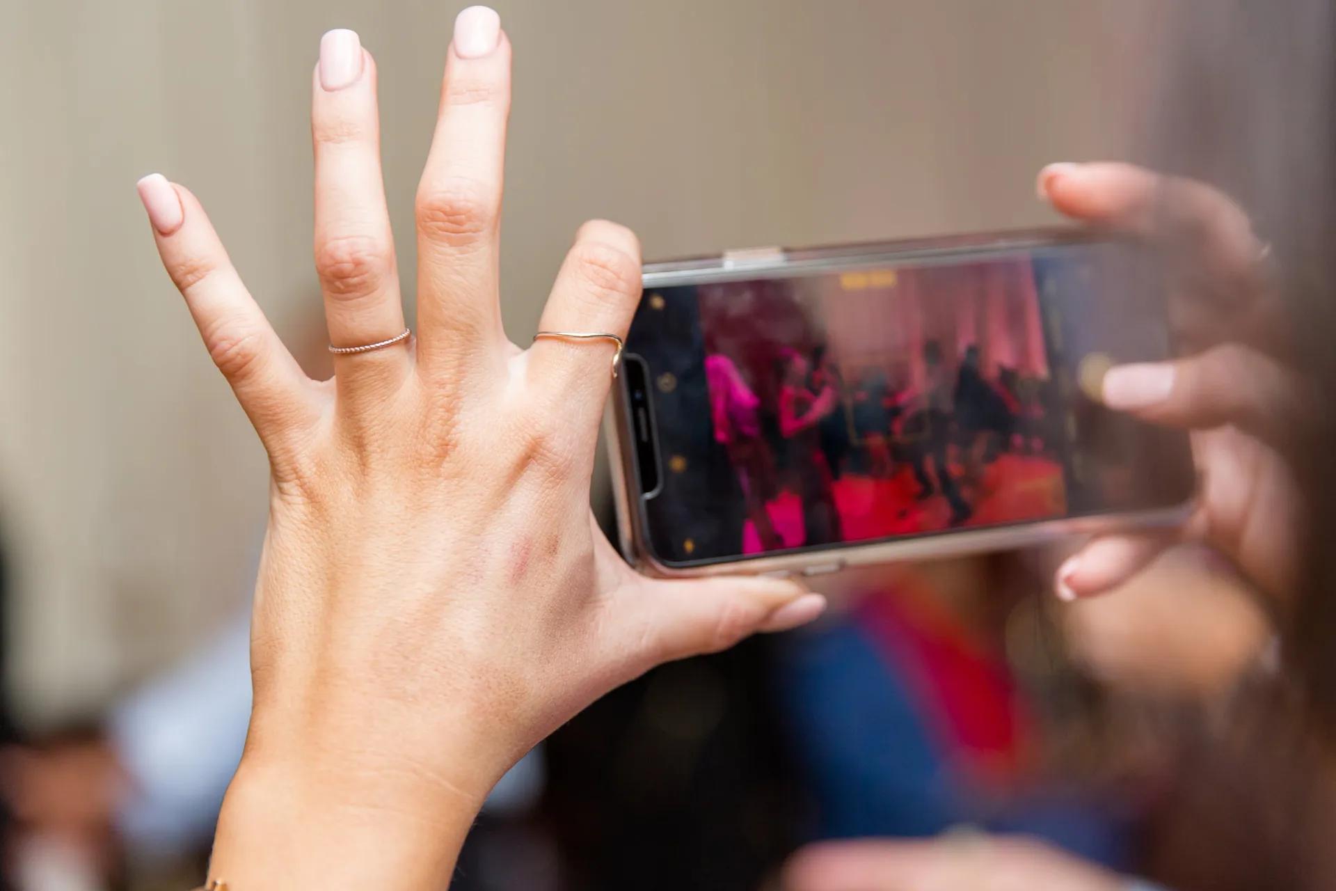 Hands raising a phone to capture the pink-lit dance floor at a corporate party.
