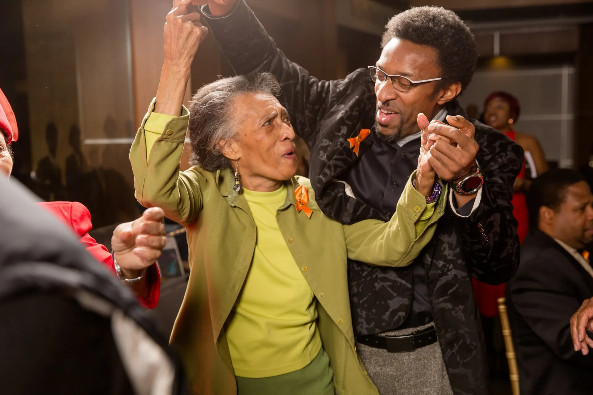 An elder in green dancing with a younger man at a community MLK celebration.