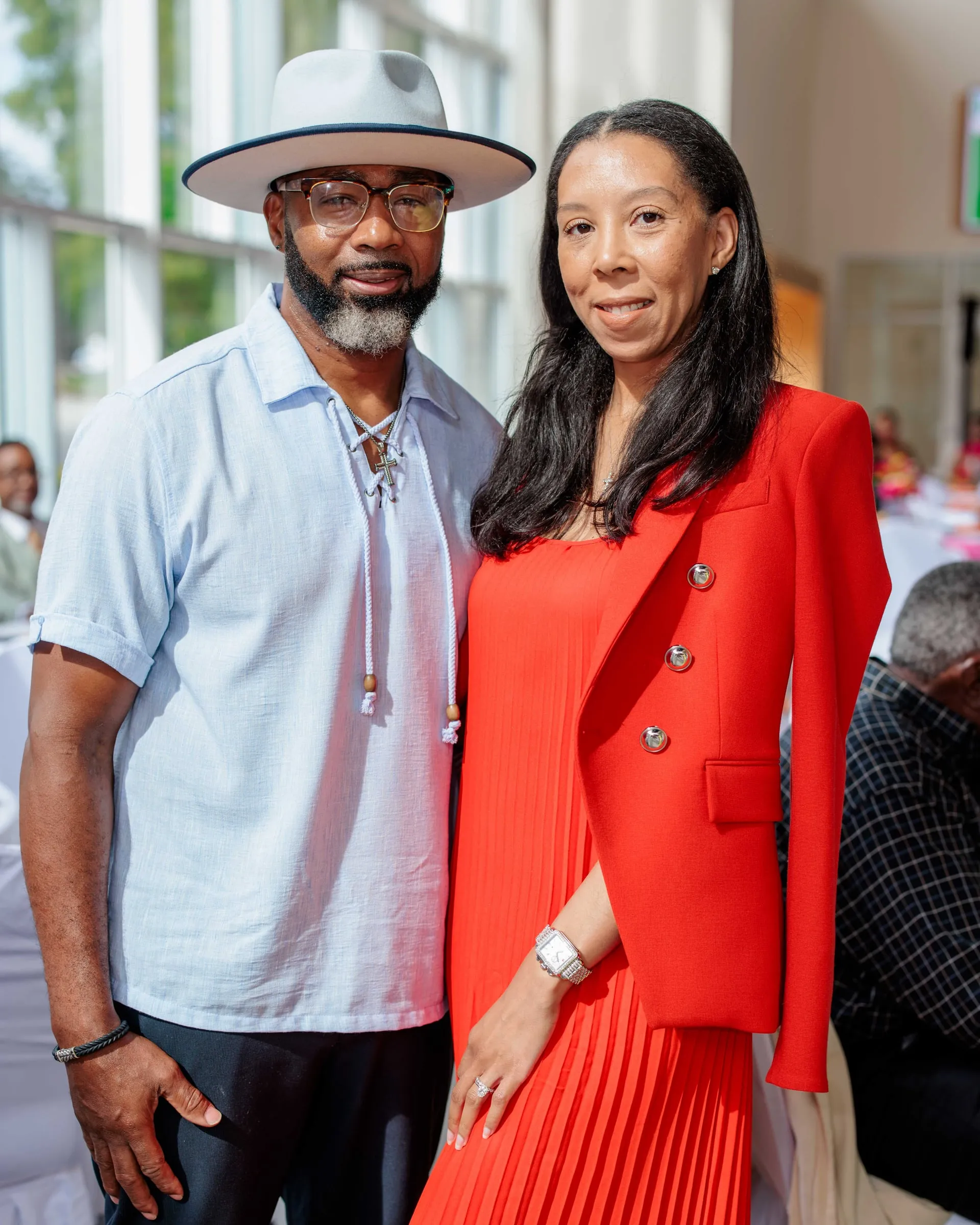 A soirée couple, he in a white brimmed hat, she in a red pleated suit.