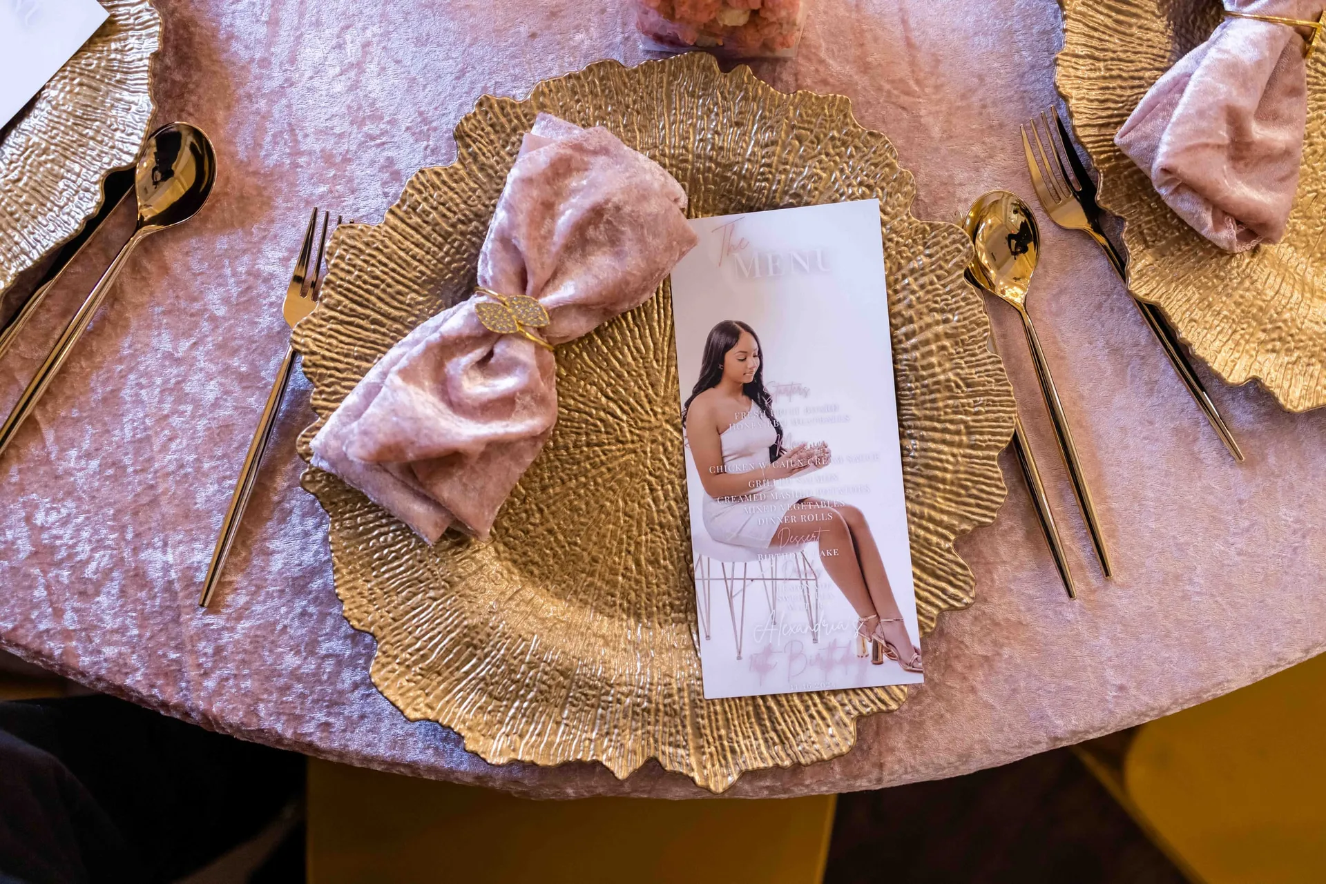 A gold charger, pink velvet bow and printed menu card at a sweet-sixteen table.