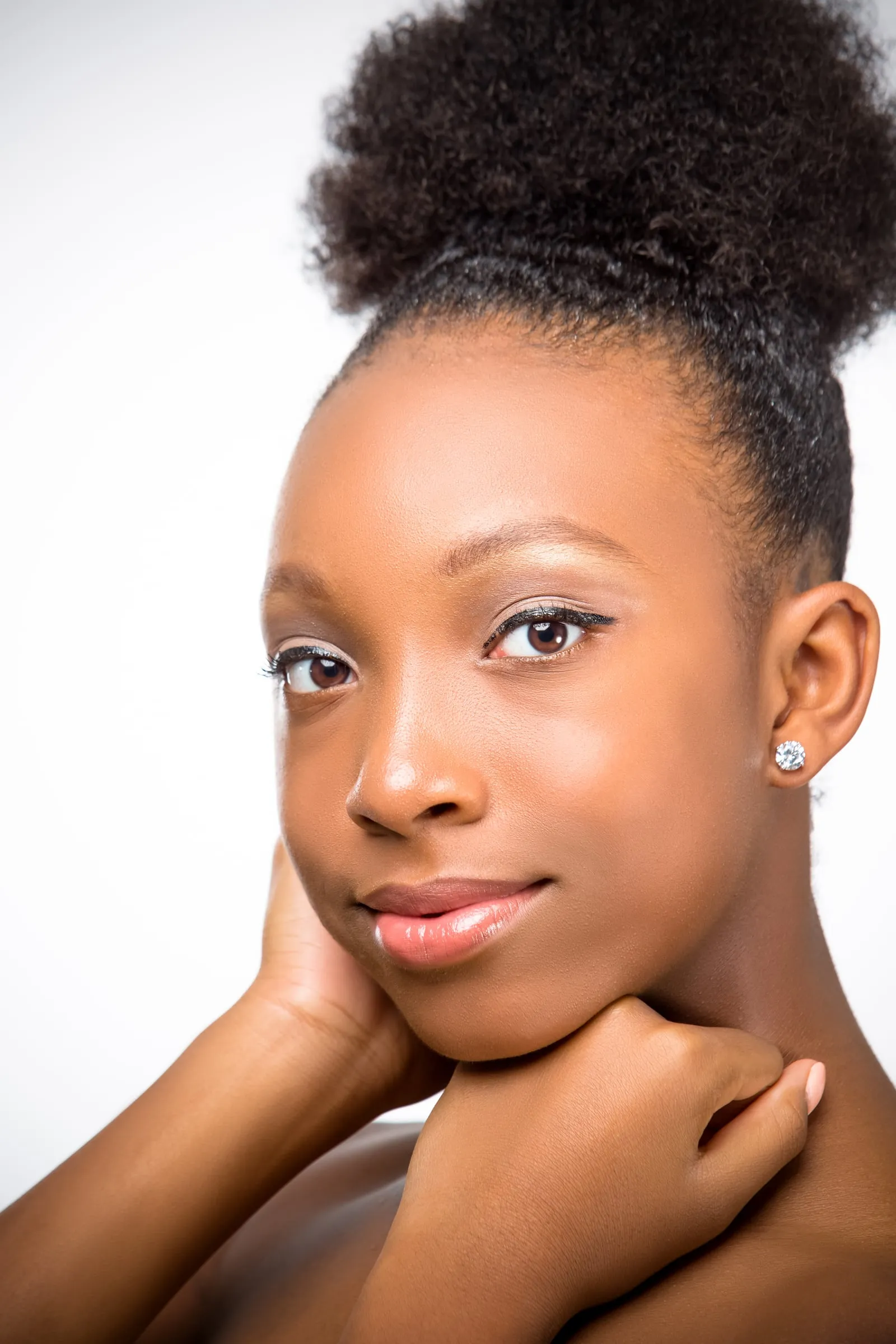 A beauty headshot of a young woman with a natural updo, chin resting on her hands.