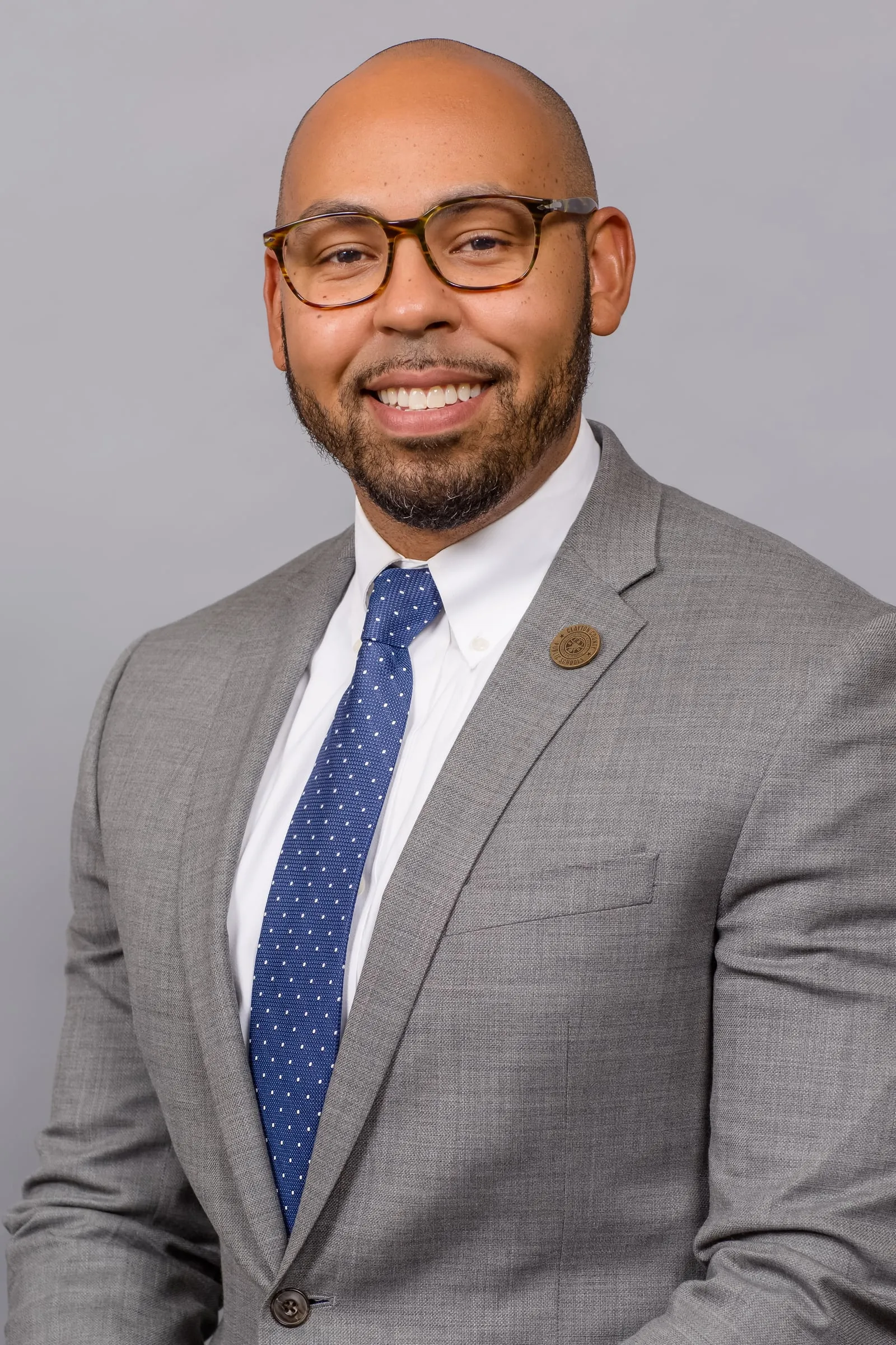 A corporate headshot of a man in glasses, a grey suit and a polka-dot tie.