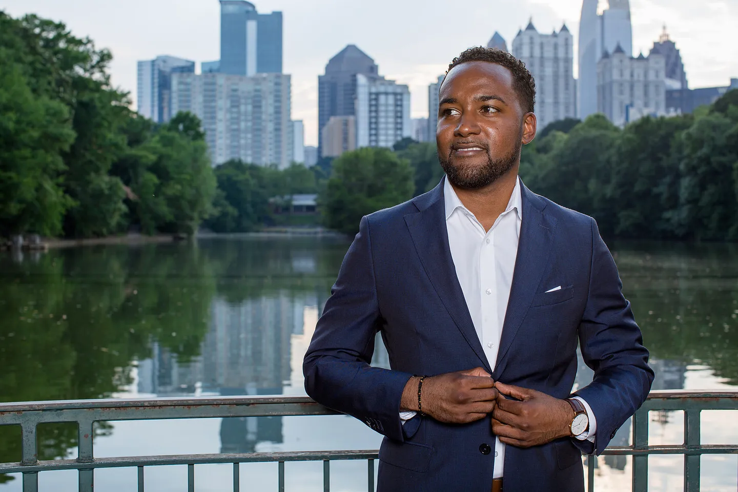 Headshot of a man in a navy suit at Piedmont Park with the Atlanta skyline behind.